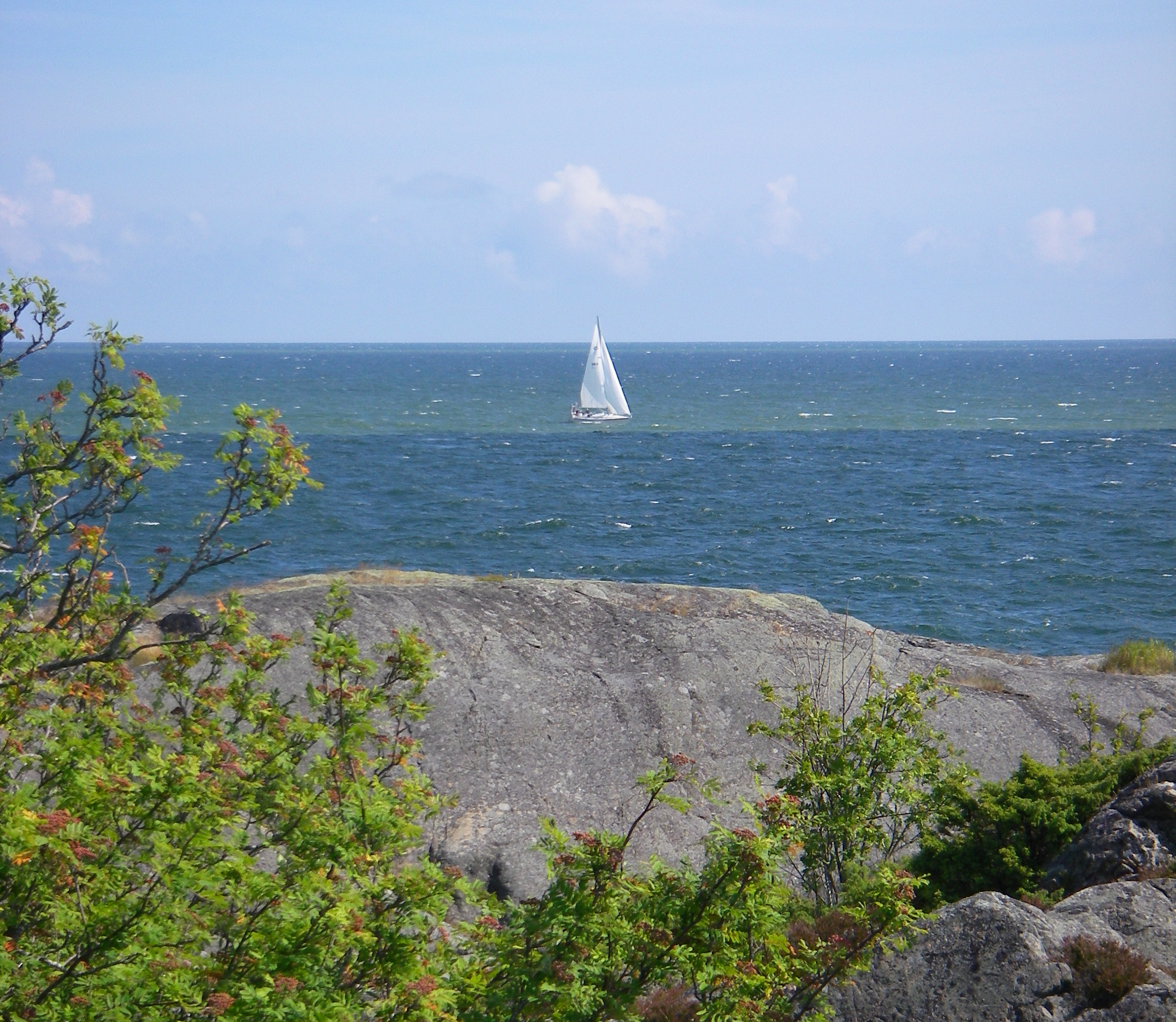 Segelbåt på havet, skärgårdsklippor i förgrunden